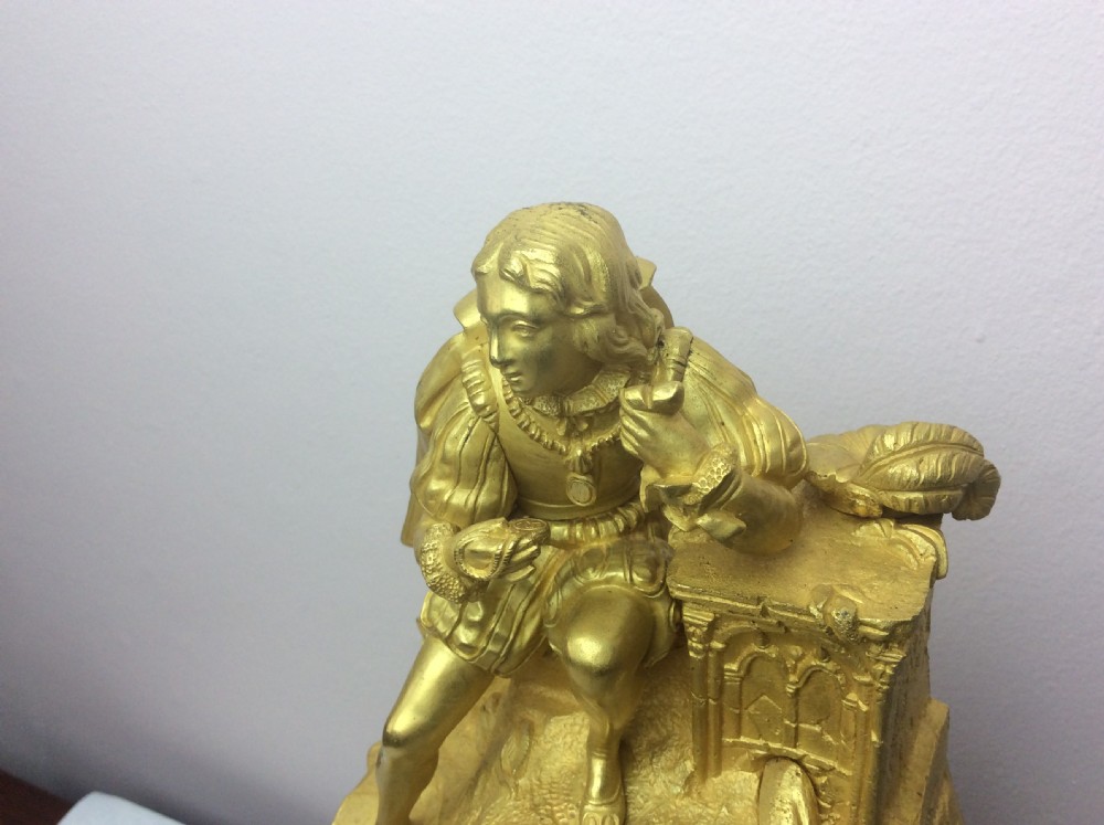 A gilt bronze French Empire mantel clock featuring a sculpted explorer figure sitting above a silvered dial on an ornate scrollwork base. View VII