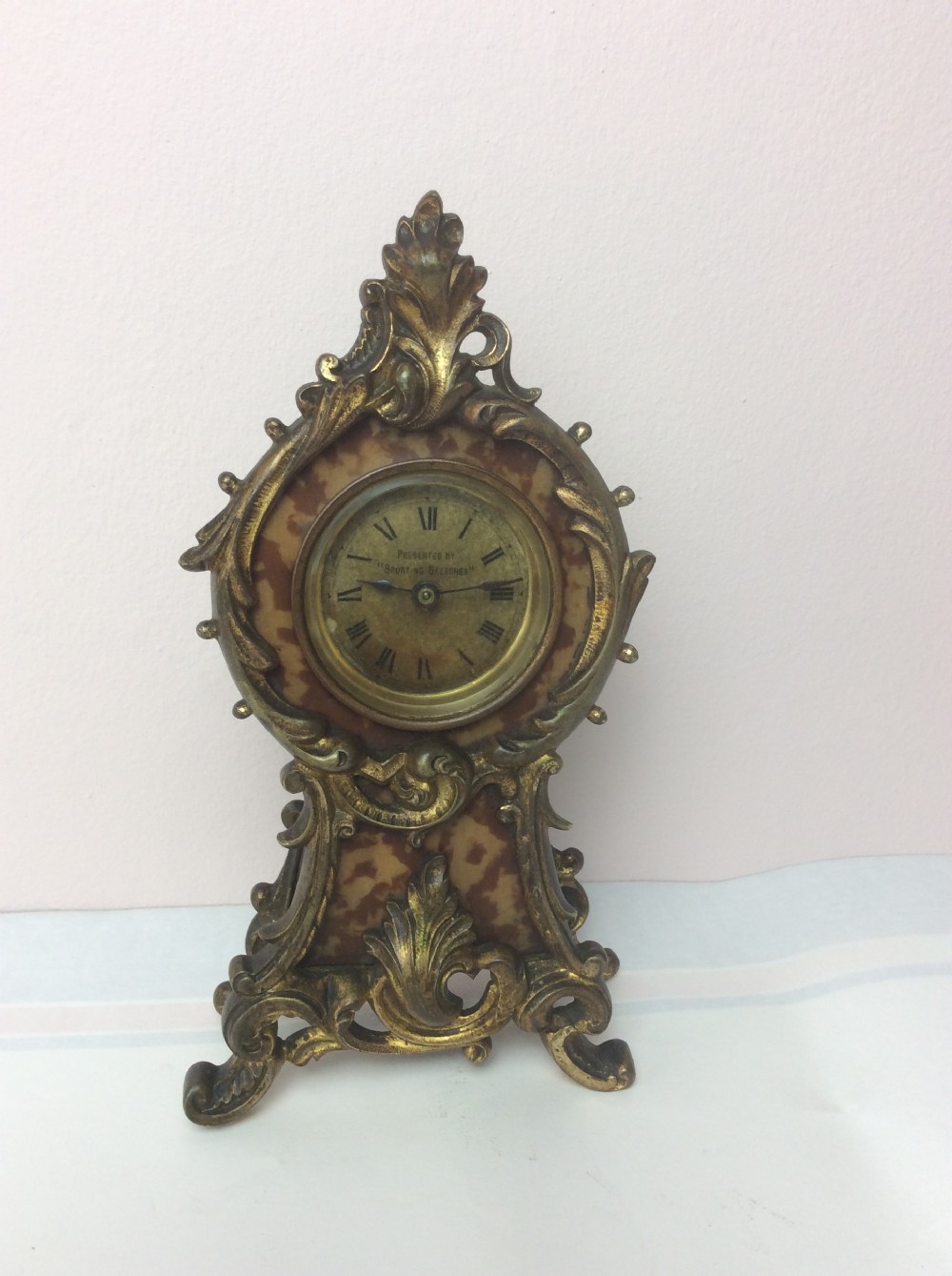 A petite late 19th-century Rococo Revival style gilt ormolu boudoir clock with faux tortoiseshell panel inserts and a circular Roman numeral dial.