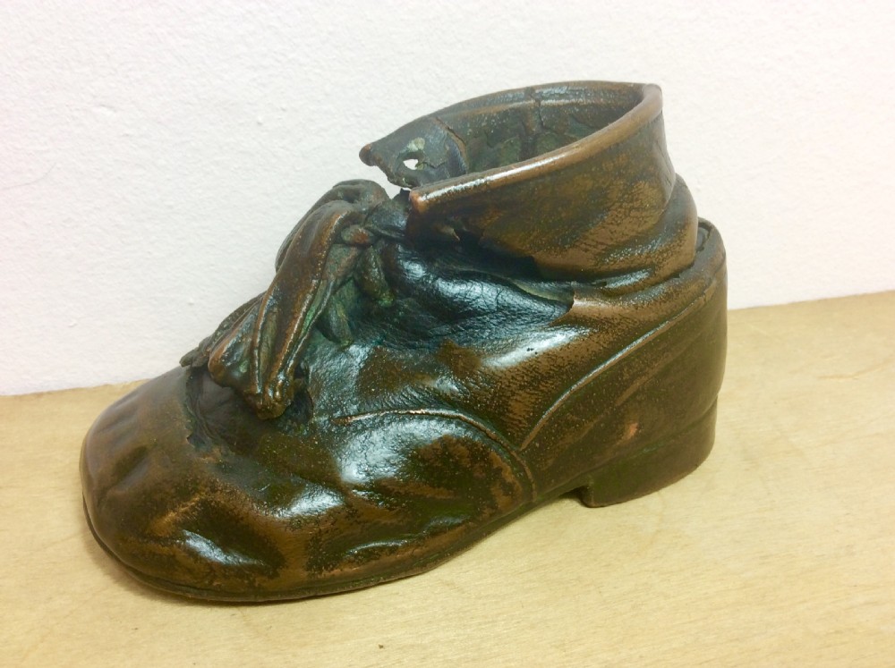 An early twentieth-century infant leather shoe preserved with an electroplated copper coating, featuring tied laces and creased detail.