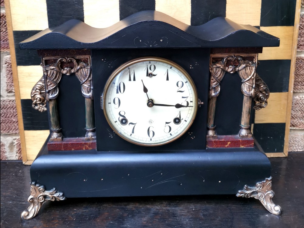 An antique late 19th-century ebonised black wooden mantel clock featuring a serpentine shaped top, gilt metal architectural columns, and ornate scroll feet.