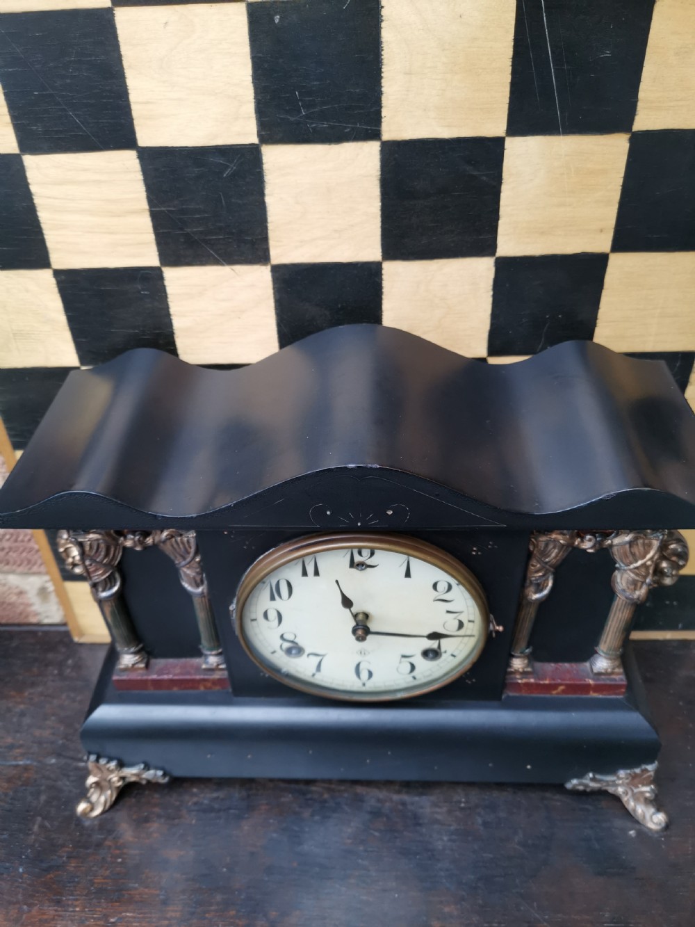 An antique late 19th-century ebonised black wooden mantel clock featuring a serpentine shaped top, gilt metal architectural columns, and ornate scroll feet. View VI