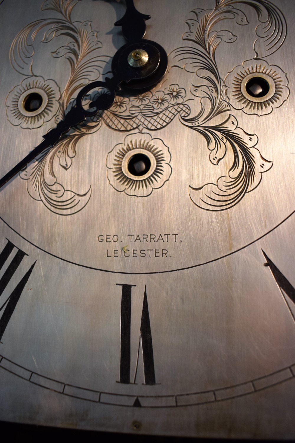 An antique dark mahogany longcase clock featuring an arched hood, engraved silvered dial with Roman numerals, and side fretwork sound apertures. View III