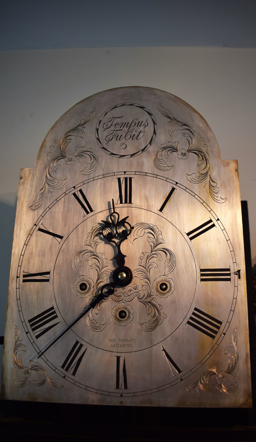 An antique dark mahogany longcase clock featuring an arched hood, engraved silvered dial with Roman numerals, and side fretwork sound apertures. View VIII