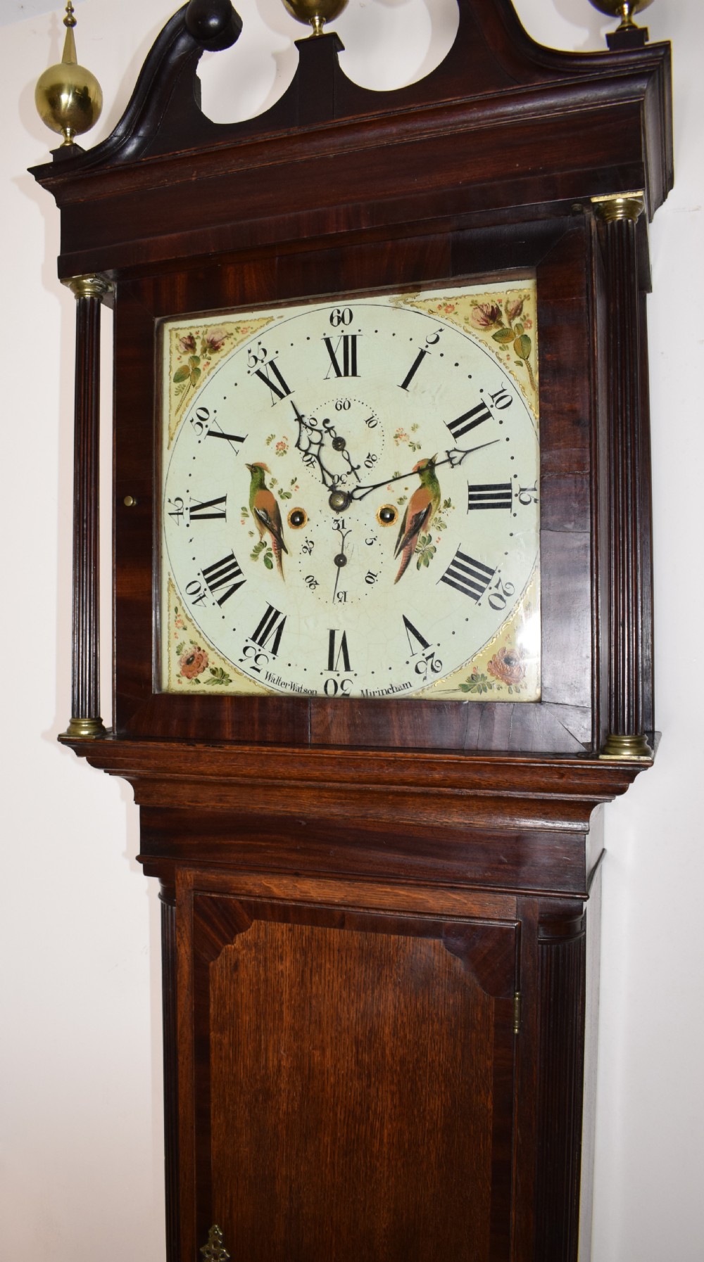 A Georgian oak and mahogany crossbanded longcase clock featuring a swan-neck pediment, brass finials, reeded columns, and a hand-painted dial with bird decoration.