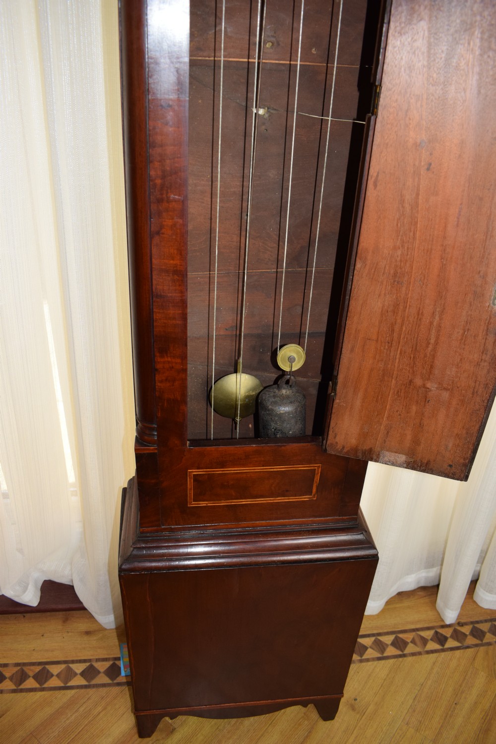 An early 19th-century Georgian flame mahogany longcase clock featuring a swan-neck pediment, brass patera, turned columns, and a hand-painted dial depicting a pastoral scene with Roman numerals. View XIII
