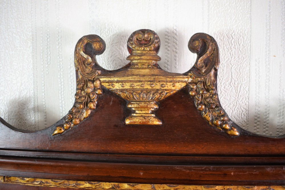 A 19th-century mahogany wall mirror featuring a bevelled oval glass plate, scroll fretwork border, gilded urn finial, and shell marquetry inlay. View II