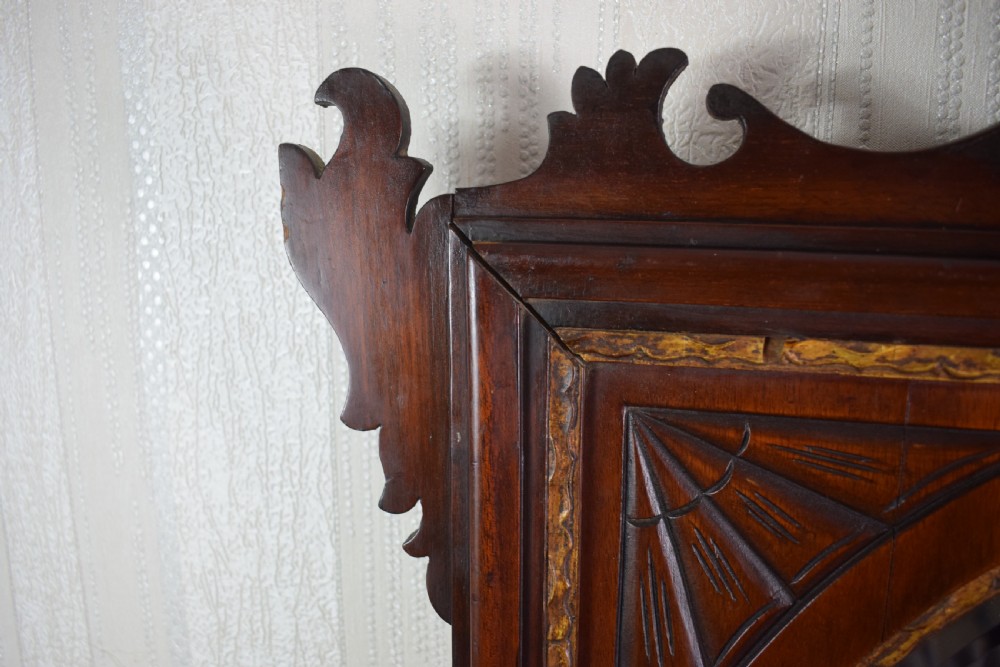 A 19th-century mahogany wall mirror featuring a bevelled oval glass plate, scroll fretwork border, gilded urn finial, and shell marquetry inlay. View V