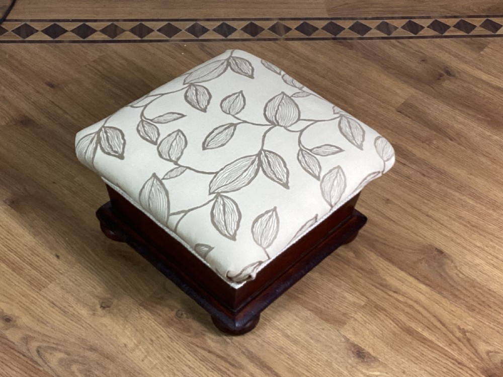 A square Victorian footstool featuring a dark mahogany plinth with turned bun feet and cream upholstery patterned with leaves. View II