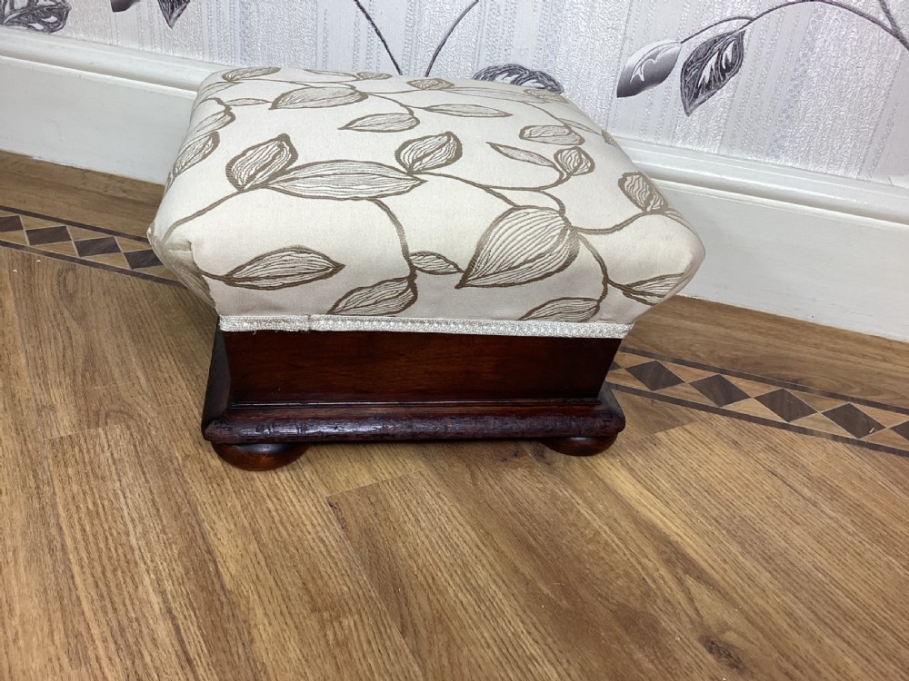 A square Victorian footstool featuring a dark mahogany plinth with turned bun feet and cream upholstery patterned with leaves. View III