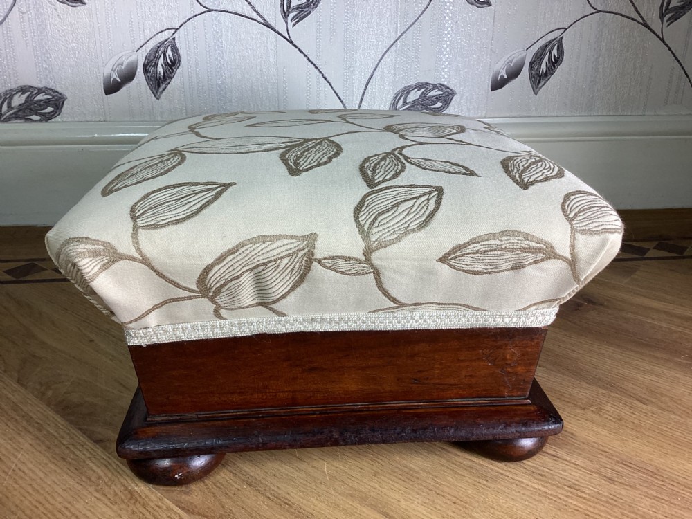 A square Victorian footstool featuring a dark mahogany plinth with turned bun feet and cream upholstery patterned with leaves. View V