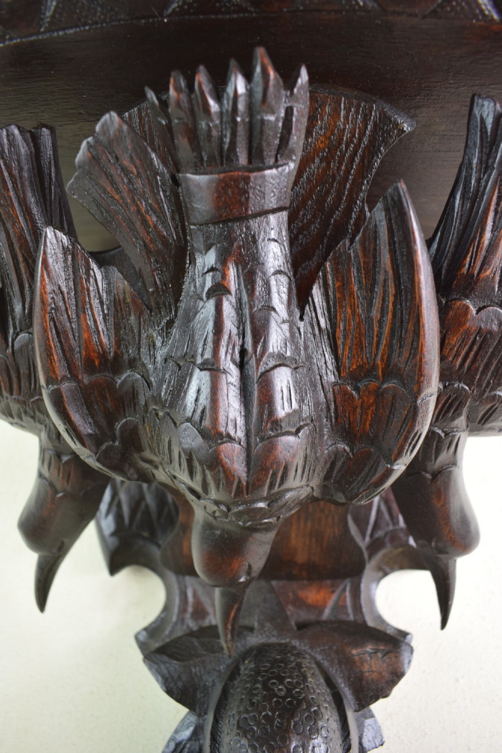 A close-up shot of a dark stained pine Black Forest wall bracket featuring intricately carved birds, fruit, and foliage.