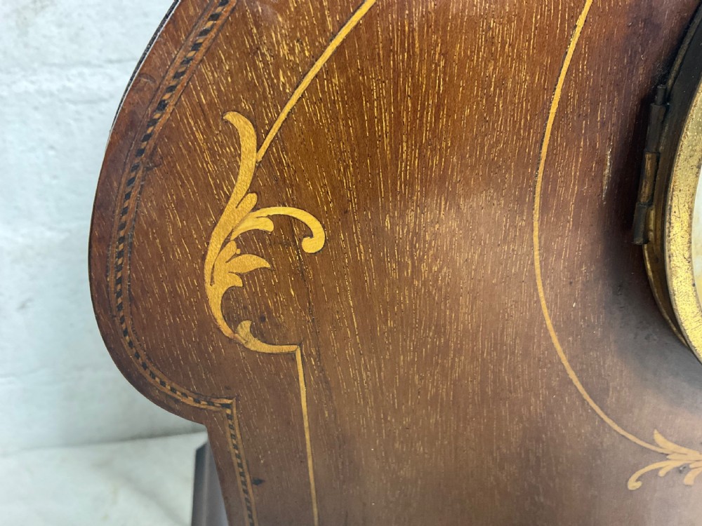 An Edwardian arched mahogany mantel clock featuring marquetry inlay, a circular brass-rimmed dial with Roman numerals, and a silver presentation plaque on the base. View II