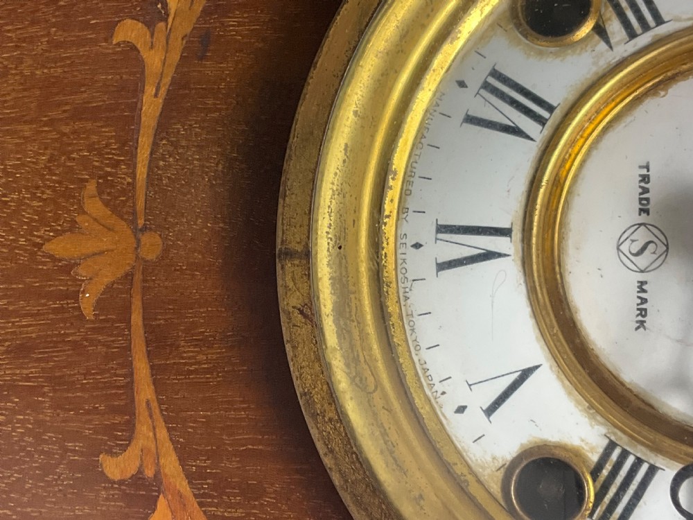 An Edwardian arched mahogany mantel clock featuring marquetry inlay, a circular brass-rimmed dial with Roman numerals, and a silver presentation plaque on the base. View III