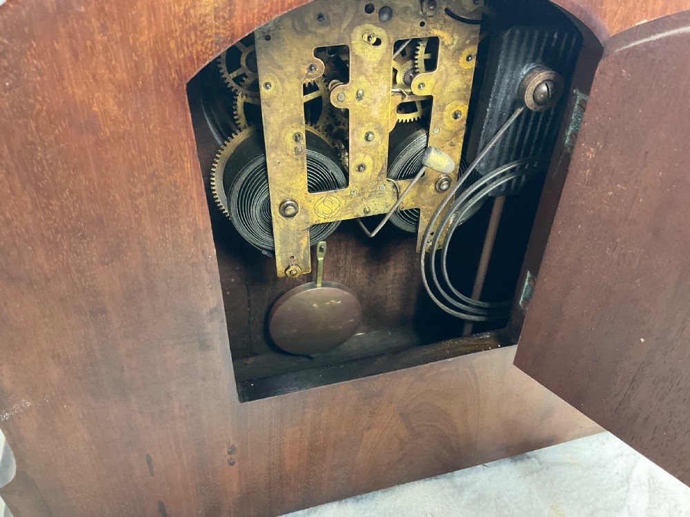 An Edwardian arched mahogany mantel clock featuring marquetry inlay, a circular brass-rimmed dial with Roman numerals, and a silver presentation plaque on the base. View IV