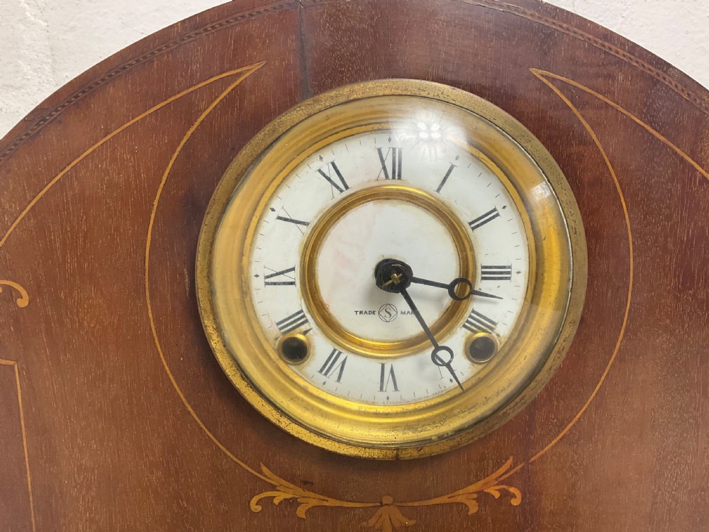 An Edwardian arched mahogany mantel clock featuring marquetry inlay, a circular brass-rimmed dial with Roman numerals, and a silver presentation plaque on the base. View V