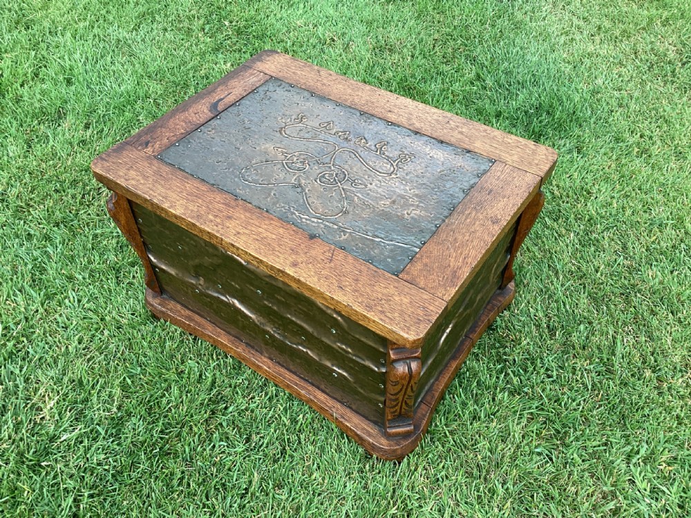 An Arts and Crafts oak log box featuring hammered copper panels with decorative repousse detailing and riveted edges.