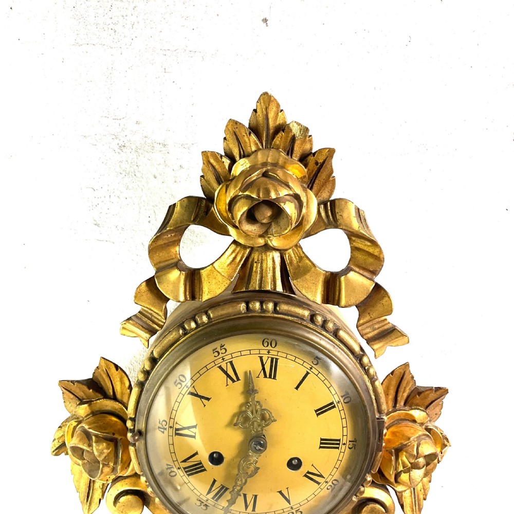 An early 20th-century giltwood cartel wall clock featuring carved floral motifs, a cream dial with Roman numerals, and ornate brass hands. View III