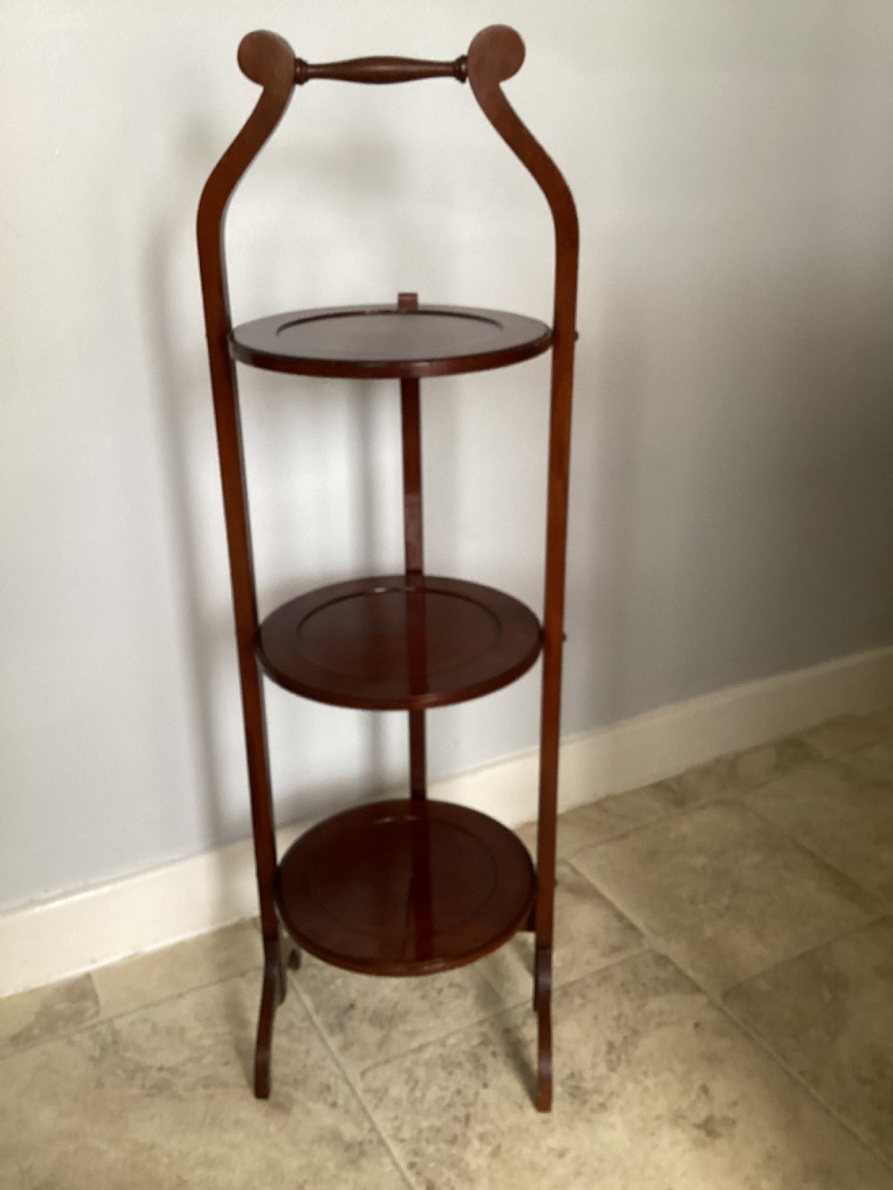 A three-tier Edwardian mahogany folding cake stand featuring circular recessed trays and a curved carrying handle at the top.