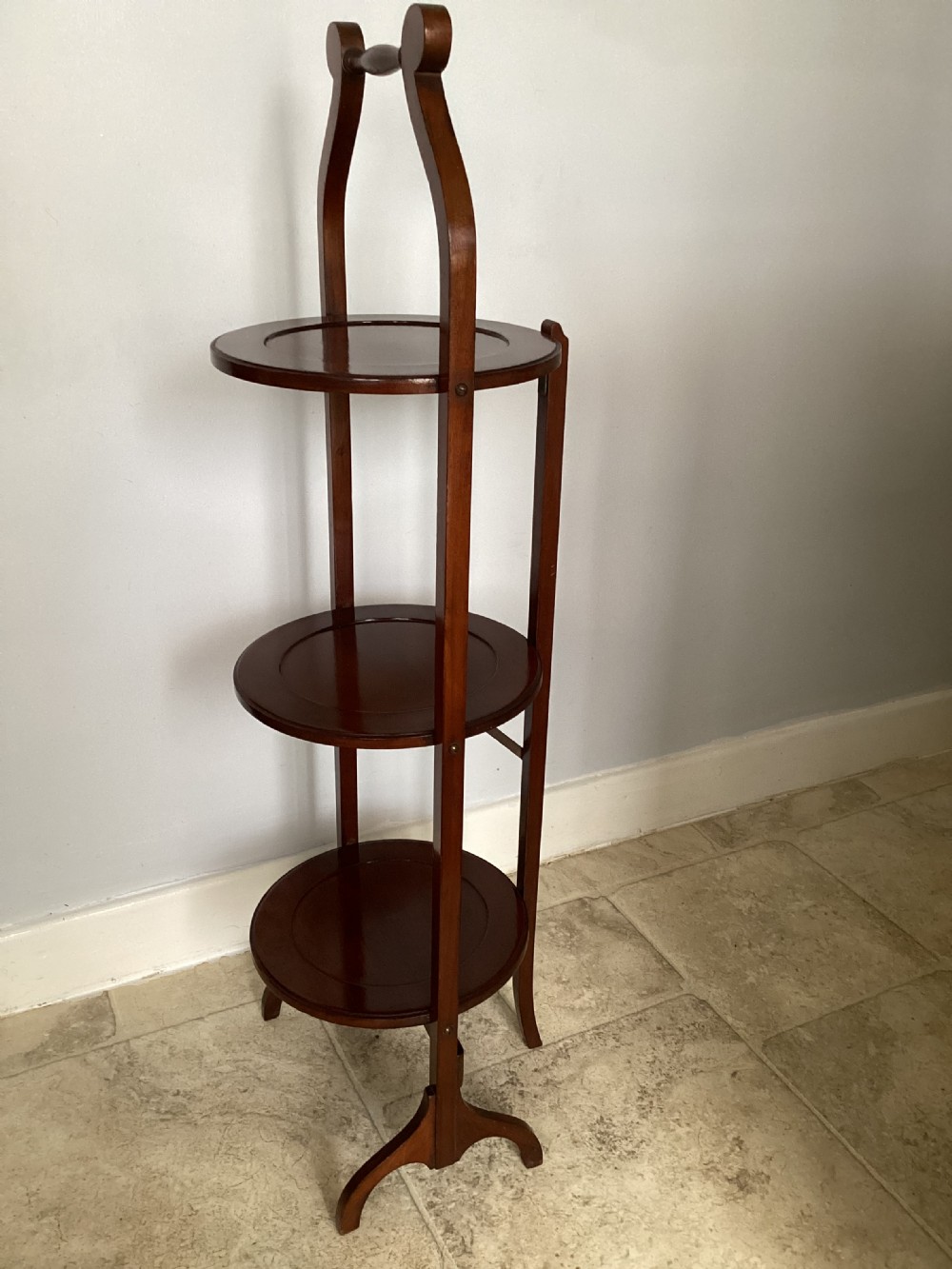 A three-tier Edwardian mahogany folding cake stand featuring circular recessed trays and a curved carrying handle at the top. View II