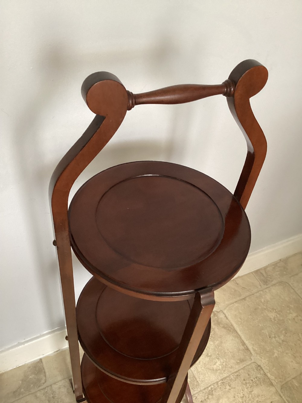 A three-tier Edwardian mahogany folding cake stand featuring circular recessed trays and a curved carrying handle at the top. View III