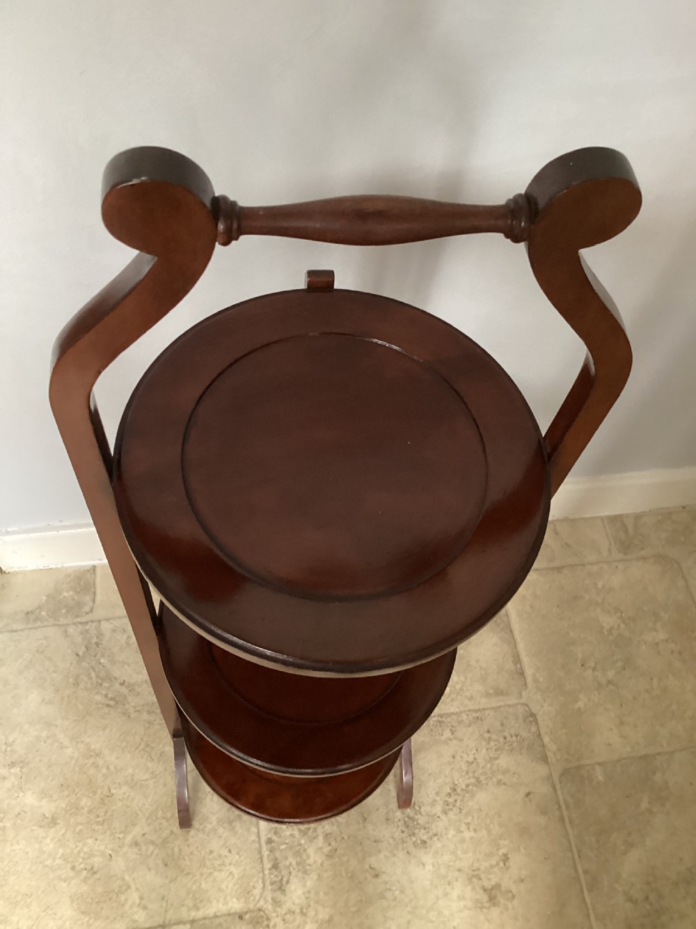 A three-tier Edwardian mahogany folding cake stand featuring circular recessed trays and a curved carrying handle at the top. View VII