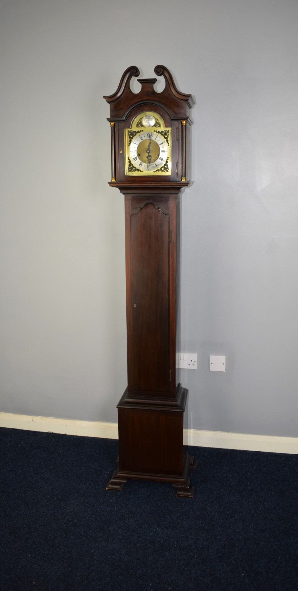 An early 20th-century slim mahogany grandmother clock featuring a swan-neck pediment, brass spandrel dial with Roman numerals, and turned side columns. View III