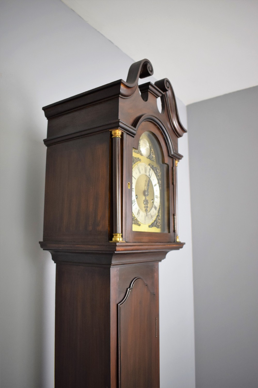 An early 20th-century slim mahogany grandmother clock featuring a swan-neck pediment, brass spandrel dial with Roman numerals, and turned side columns. View II