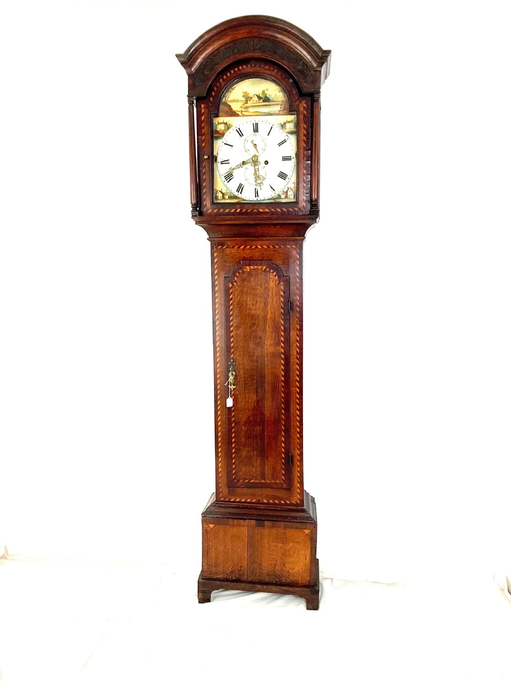 A Georgian oak longcase clock featuring a hand-painted arch dial, turned hood columns, and chequered geometric inlay. View V