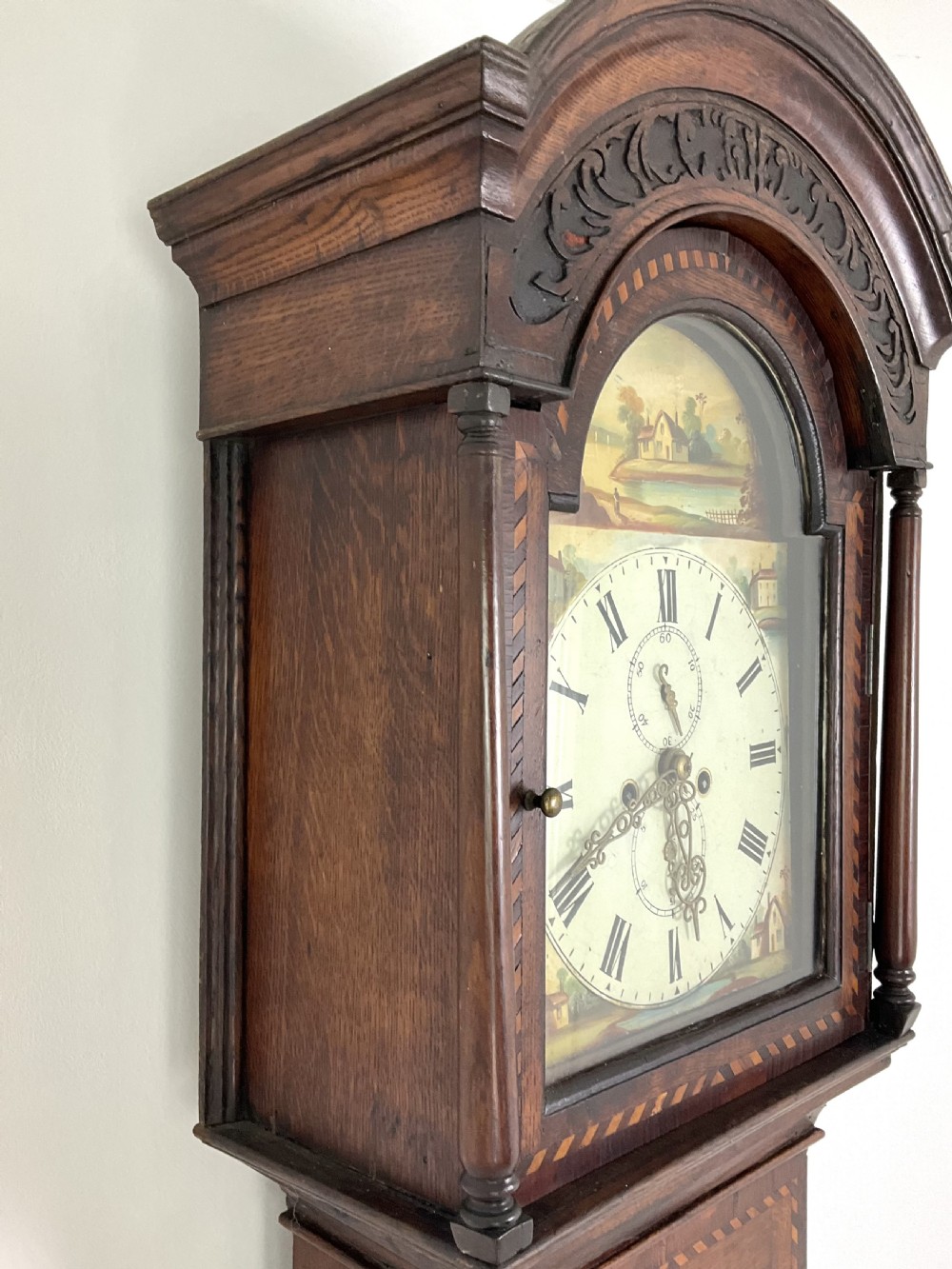 A Georgian oak longcase clock featuring a hand-painted arch dial, turned hood columns, and chequered geometric inlay. View IV