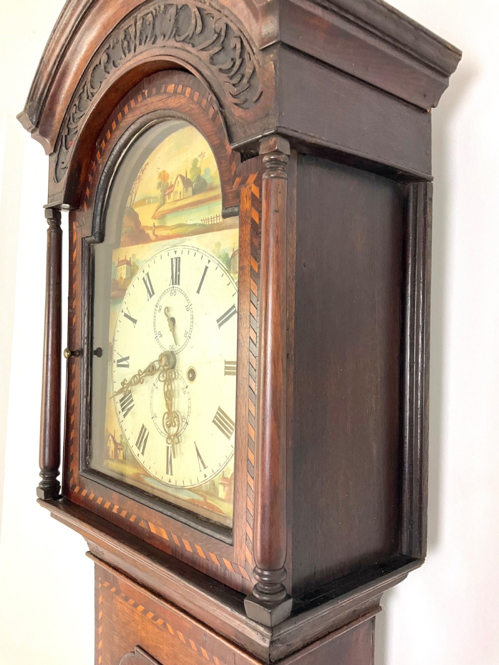 A Georgian oak longcase clock featuring a hand-painted arch dial, turned hood columns, and chequered geometric inlay.
