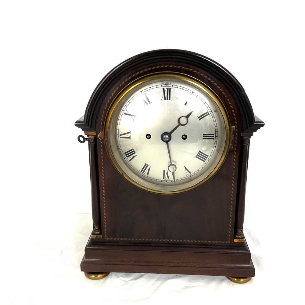 A 19th-century mahogany bracket clock featuring an arched top, brass-framed circular dial with Roman numerals, and brass turned feet.