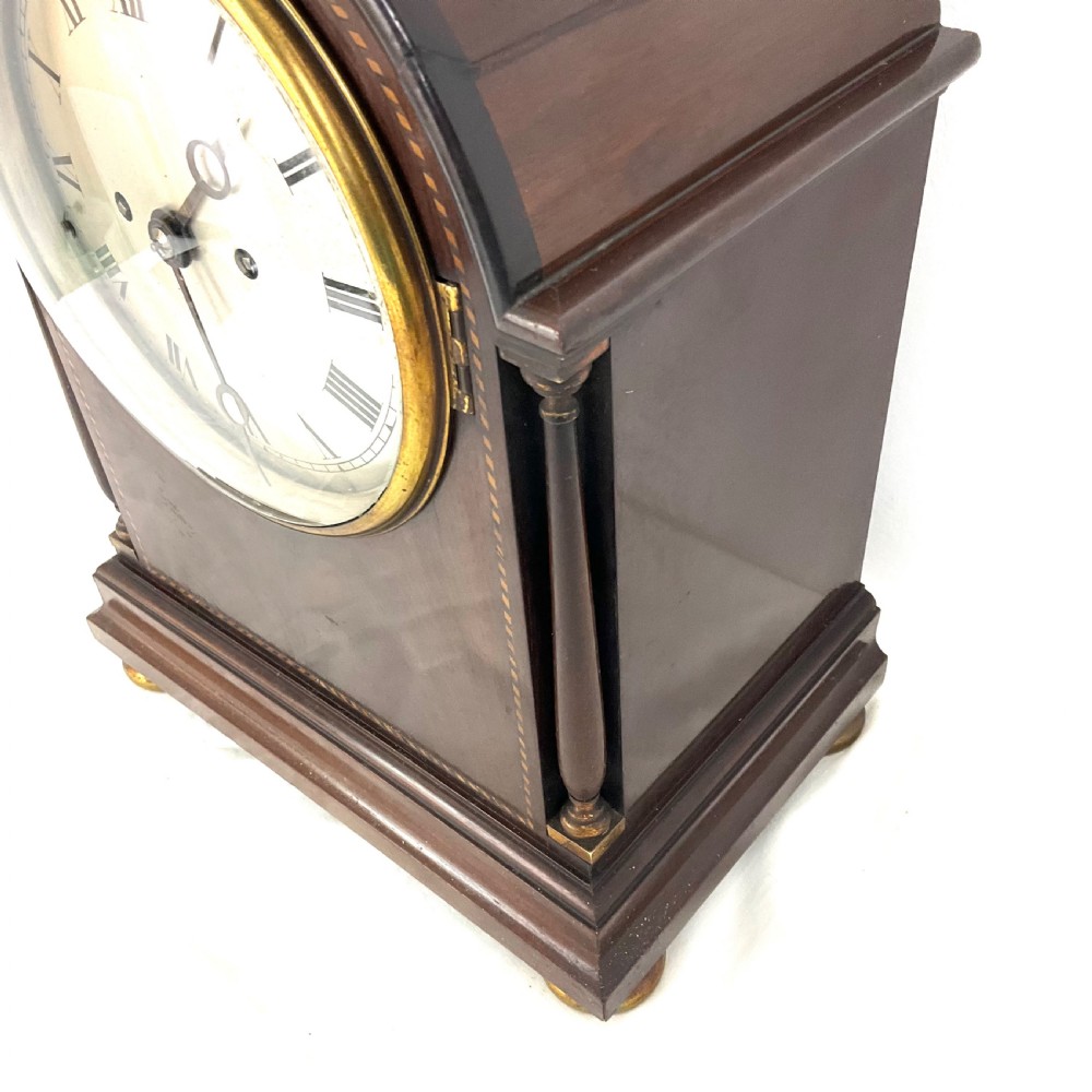 A 19th-century mahogany bracket clock featuring an arched top, brass-framed circular dial with Roman numerals, and brass turned feet. View III