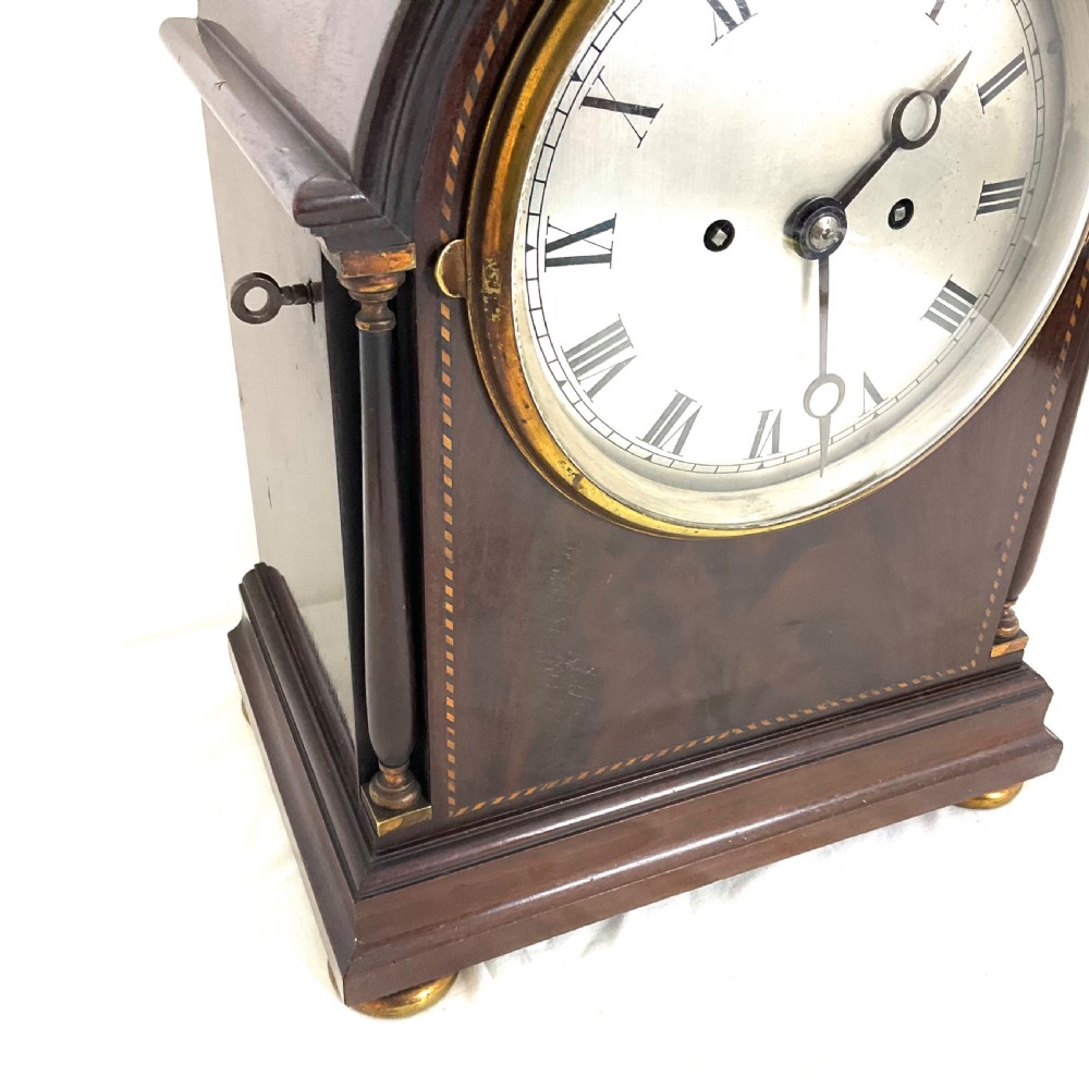 A 19th-century mahogany bracket clock featuring an arched top, brass-framed circular dial with Roman numerals, and brass turned feet. View IV