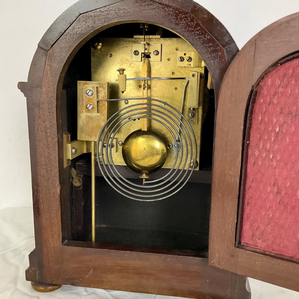 A 19th-century mahogany bracket clock featuring an arched top, brass-framed circular dial with Roman numerals, and brass turned feet. View V