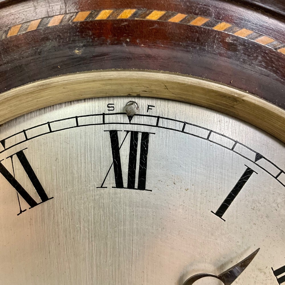 A 19th-century mahogany bracket clock featuring an arched top, brass-framed circular dial with Roman numerals, and brass turned feet. View VI