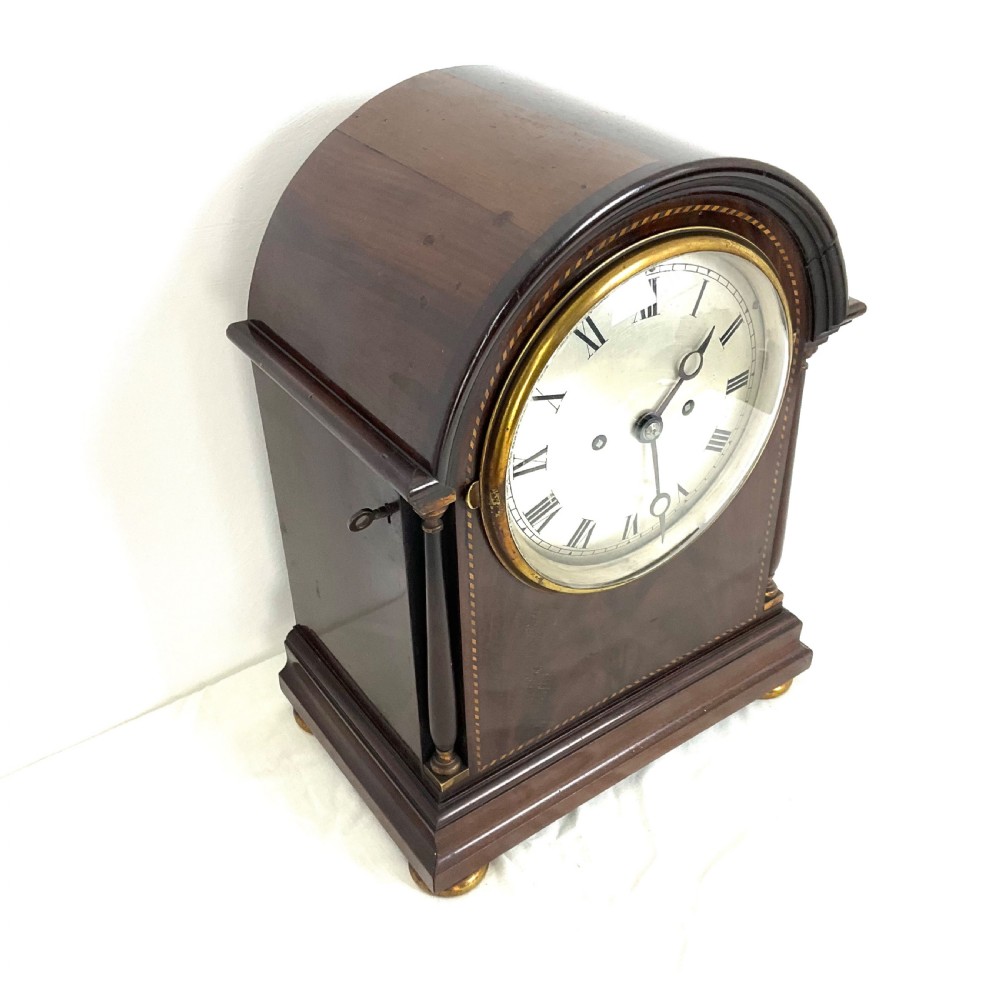 A 19th-century mahogany bracket clock featuring an arched top, brass-framed circular dial with Roman numerals, and brass turned feet. View VIII