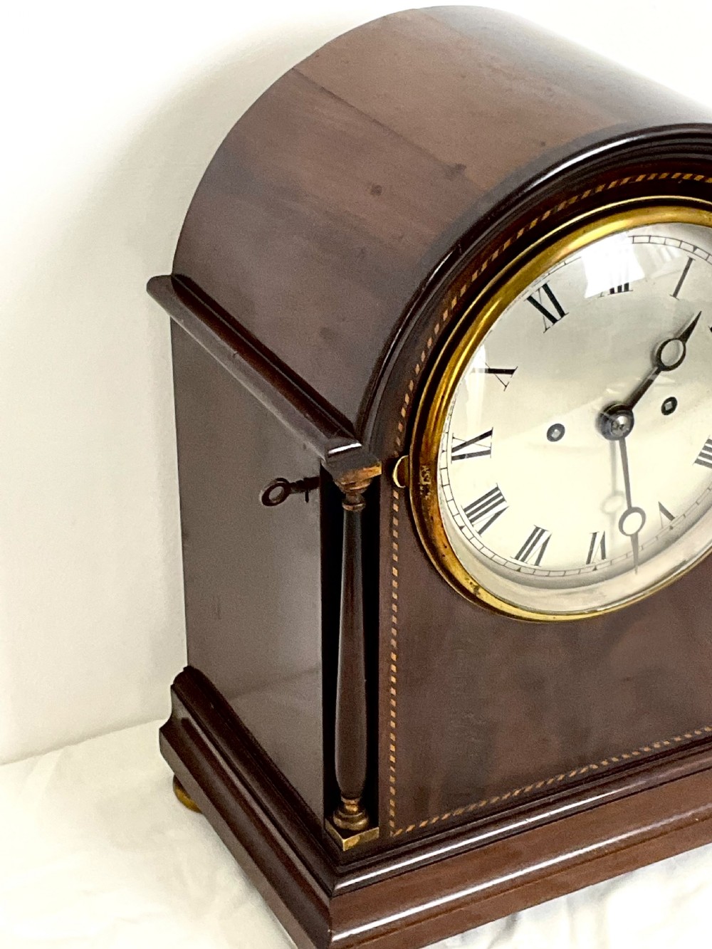 A 19th-century mahogany bracket clock featuring an arched top, brass-framed circular dial with Roman numerals, and brass turned feet. View XI