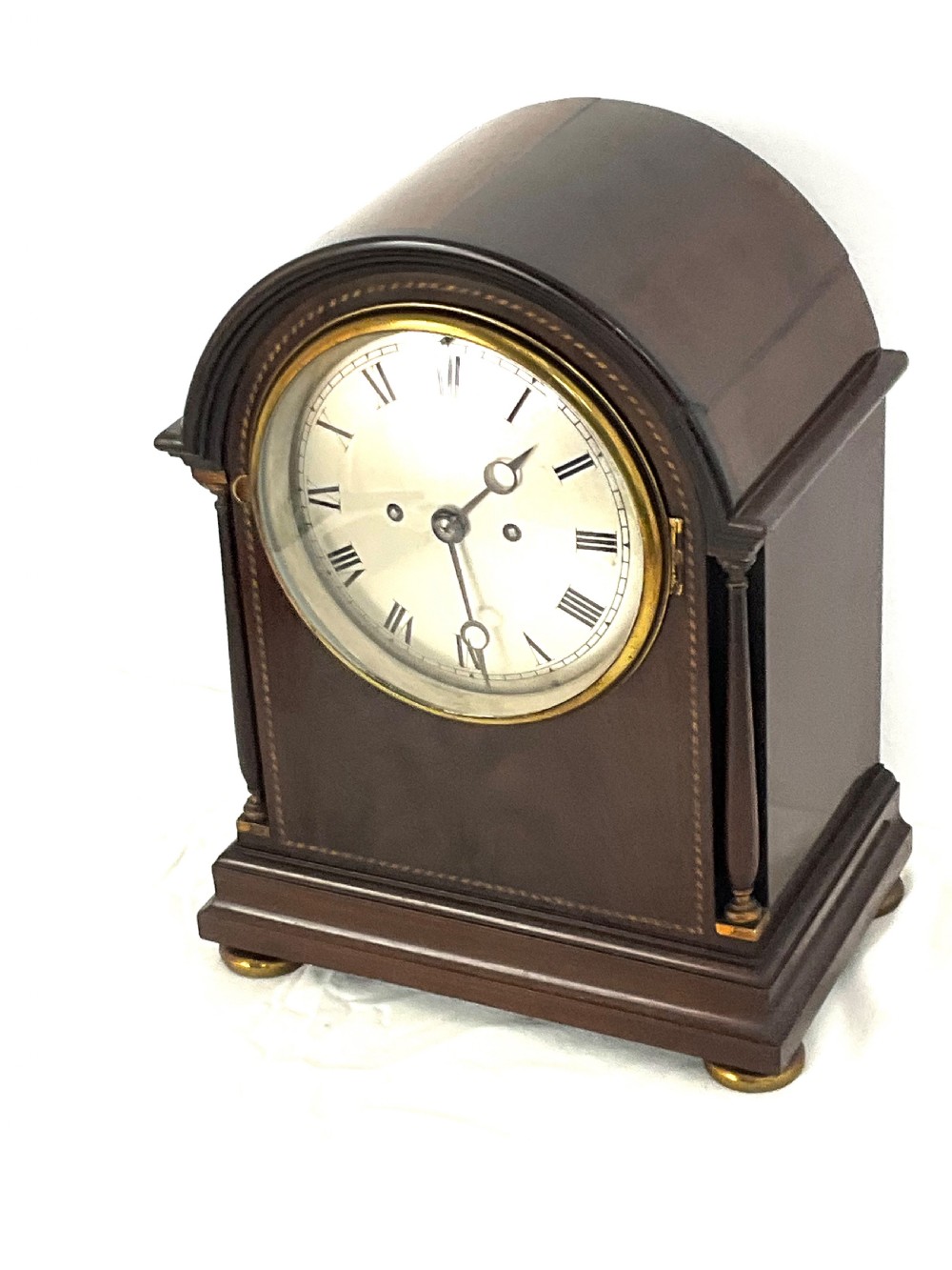 A 19th-century mahogany bracket clock featuring an arched top, brass-framed circular dial with Roman numerals, and brass turned feet. View XIII
