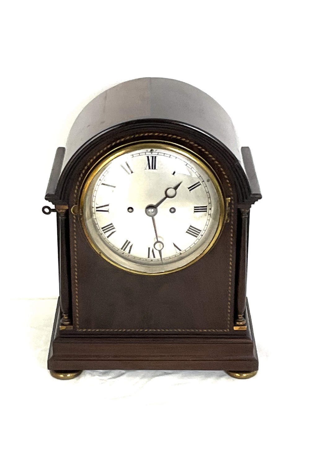 A 19th-century mahogany bracket clock featuring an arched top, brass-framed circular dial with Roman numerals, and brass turned feet. View XIV