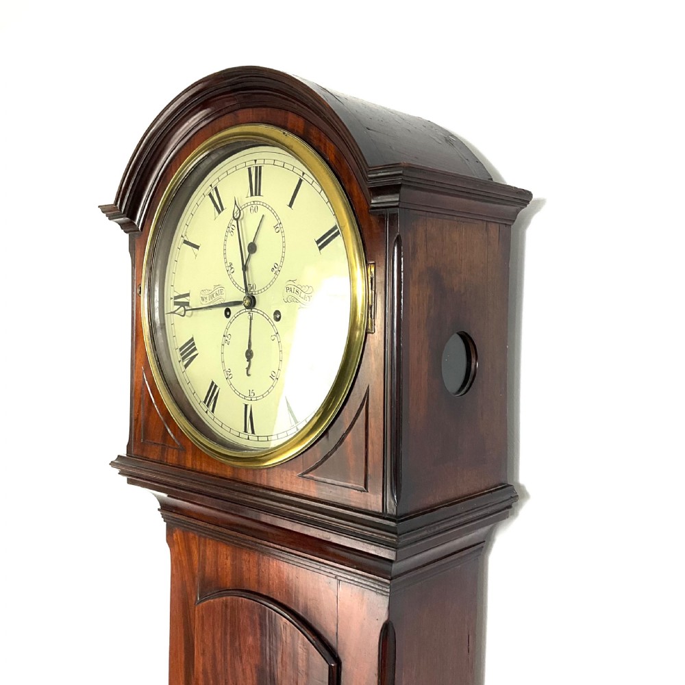 A Regency period flame mahogany longcase clock featuring a circular brass bezel, Roman numerals, subsidiary seconds display, and an arched bonnet.