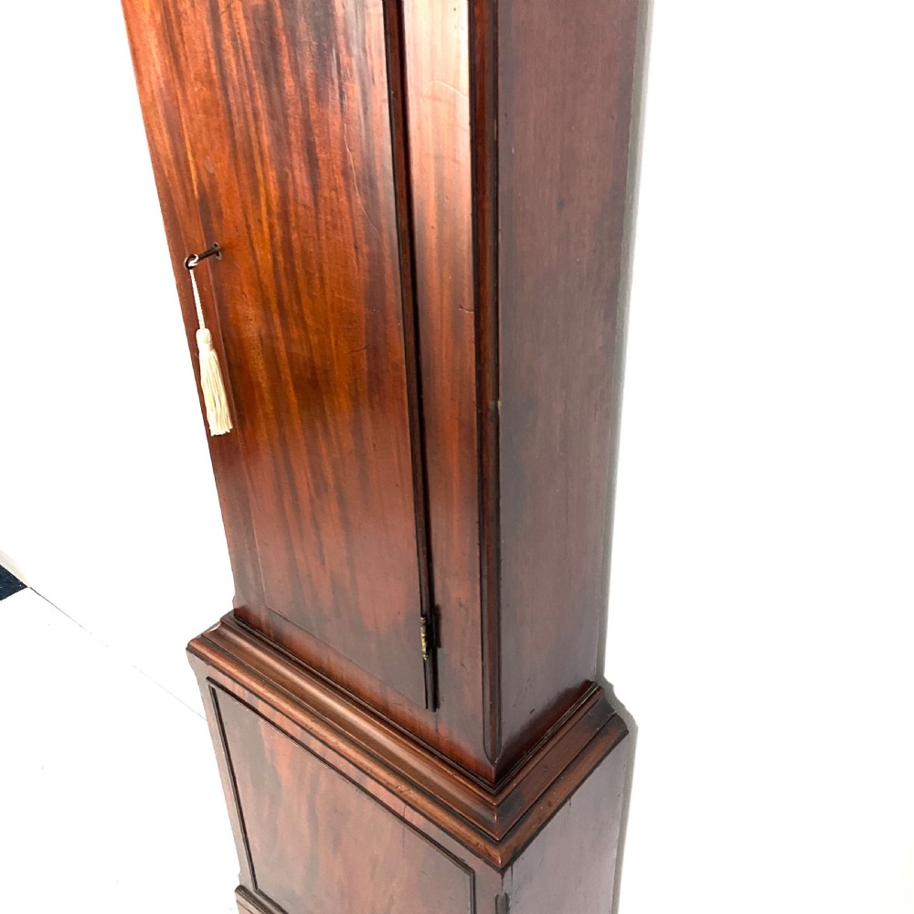 A Regency period flame mahogany longcase clock featuring a circular brass bezel, Roman numerals, subsidiary seconds display, and an arched bonnet. View IV