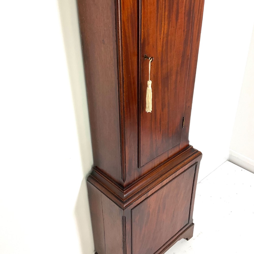 A Regency period flame mahogany longcase clock featuring a circular brass bezel, Roman numerals, subsidiary seconds display, and an arched bonnet. View VI