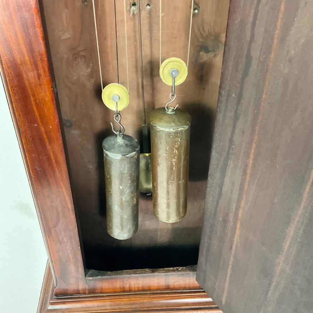 A Regency period flame mahogany longcase clock featuring a circular brass bezel, Roman numerals, subsidiary seconds display, and an arched bonnet. View VII