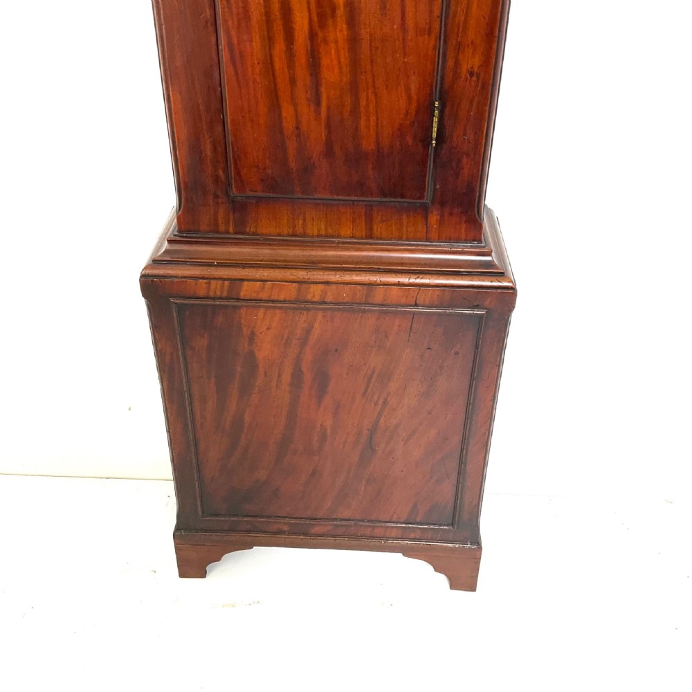 A Regency period flame mahogany longcase clock featuring a circular brass bezel, Roman numerals, subsidiary seconds display, and an arched bonnet. View VIII