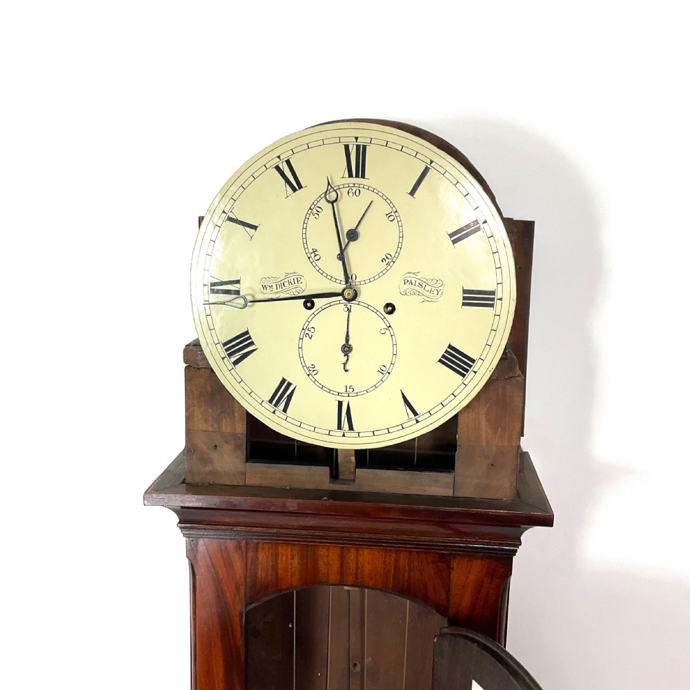 A Regency period flame mahogany longcase clock featuring a circular brass bezel, Roman numerals, subsidiary seconds display, and an arched bonnet. View IX