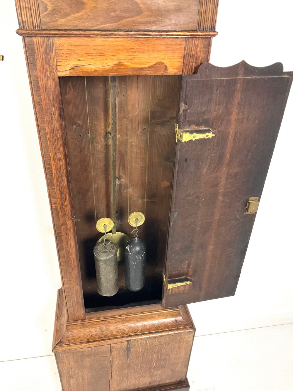 A tall Georgian oak longcase clock featuring a square painted dial, brass column accents, and a panelled wooden case. View VII