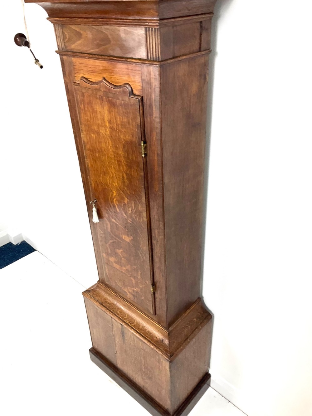 A tall Georgian oak longcase clock featuring a square painted dial, brass column accents, and a panelled wooden case. View VIII