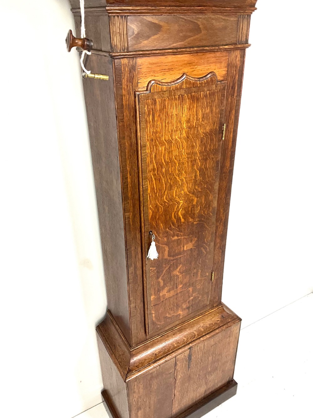 A tall Georgian oak longcase clock featuring a square painted dial, brass column accents, and a panelled wooden case. View IX
