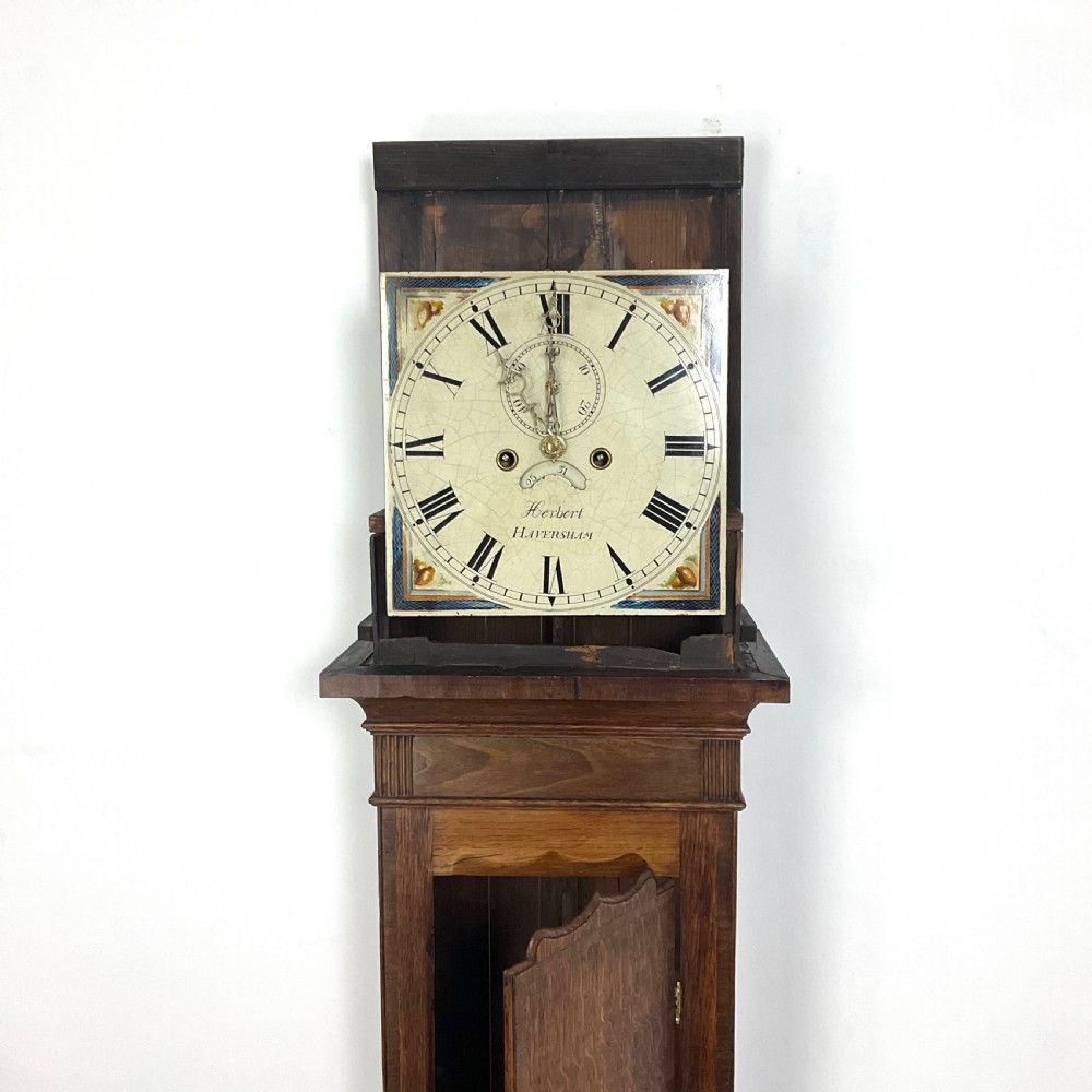 A tall Georgian oak longcase clock featuring a square painted dial, brass column accents, and a panelled wooden case. View XII