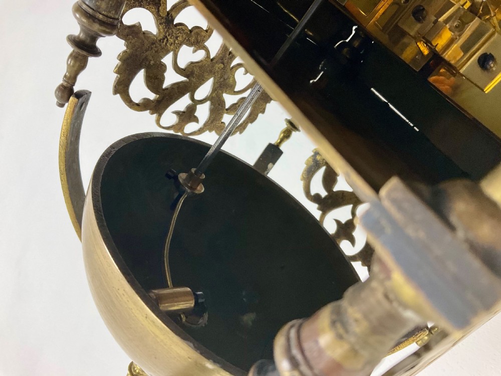 An antique brass lantern clock featuring a top-mounted bell dome, engraved foliate dial with Roman numerals, and ornate pierced frets. View VII